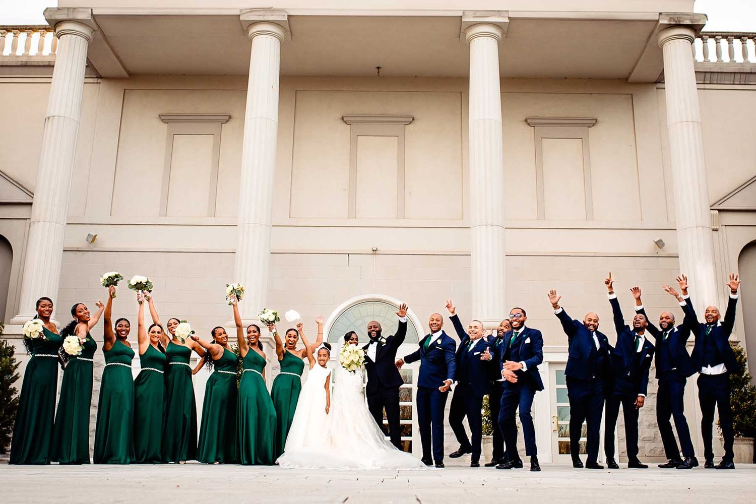 Wedding party poses in front of a grand colonial-style building with white columns.