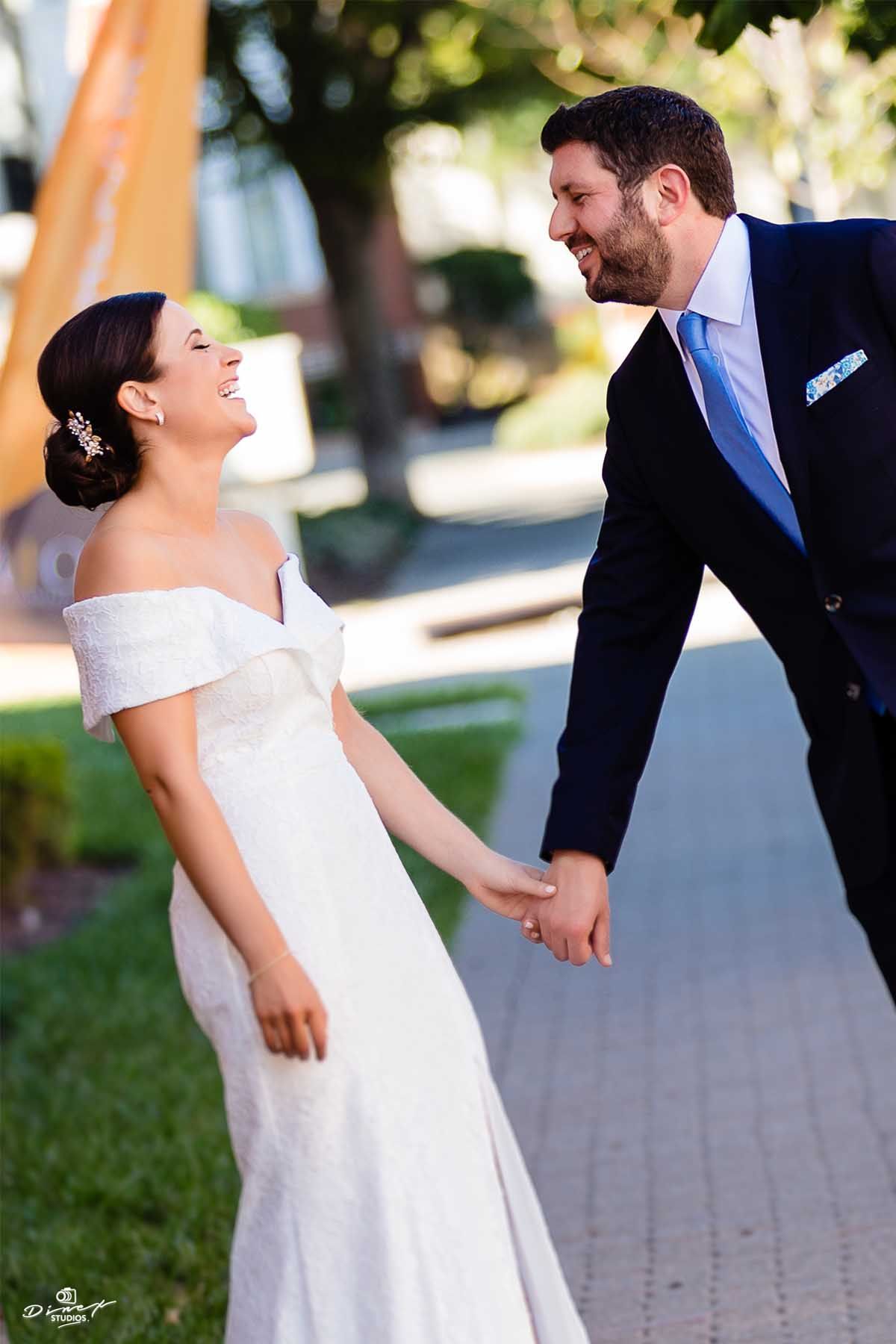 A joyful wedding couple laughing together outdoors in formal attire.