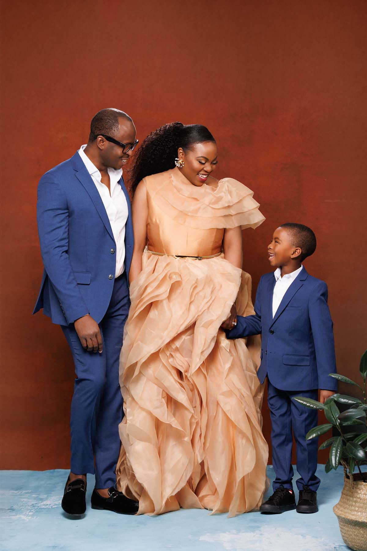Family photo with coordinated outfits against terracotta wall with greenery.
