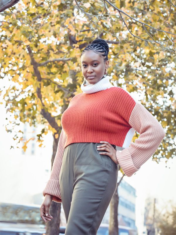 Casual autumn fashion featuring a red knit vest paired with beige sleeves and gray pants outdoors.
