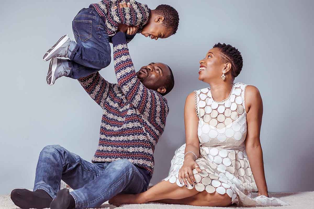 A couple shares playful moments during a studio photoshoot against a grey background.