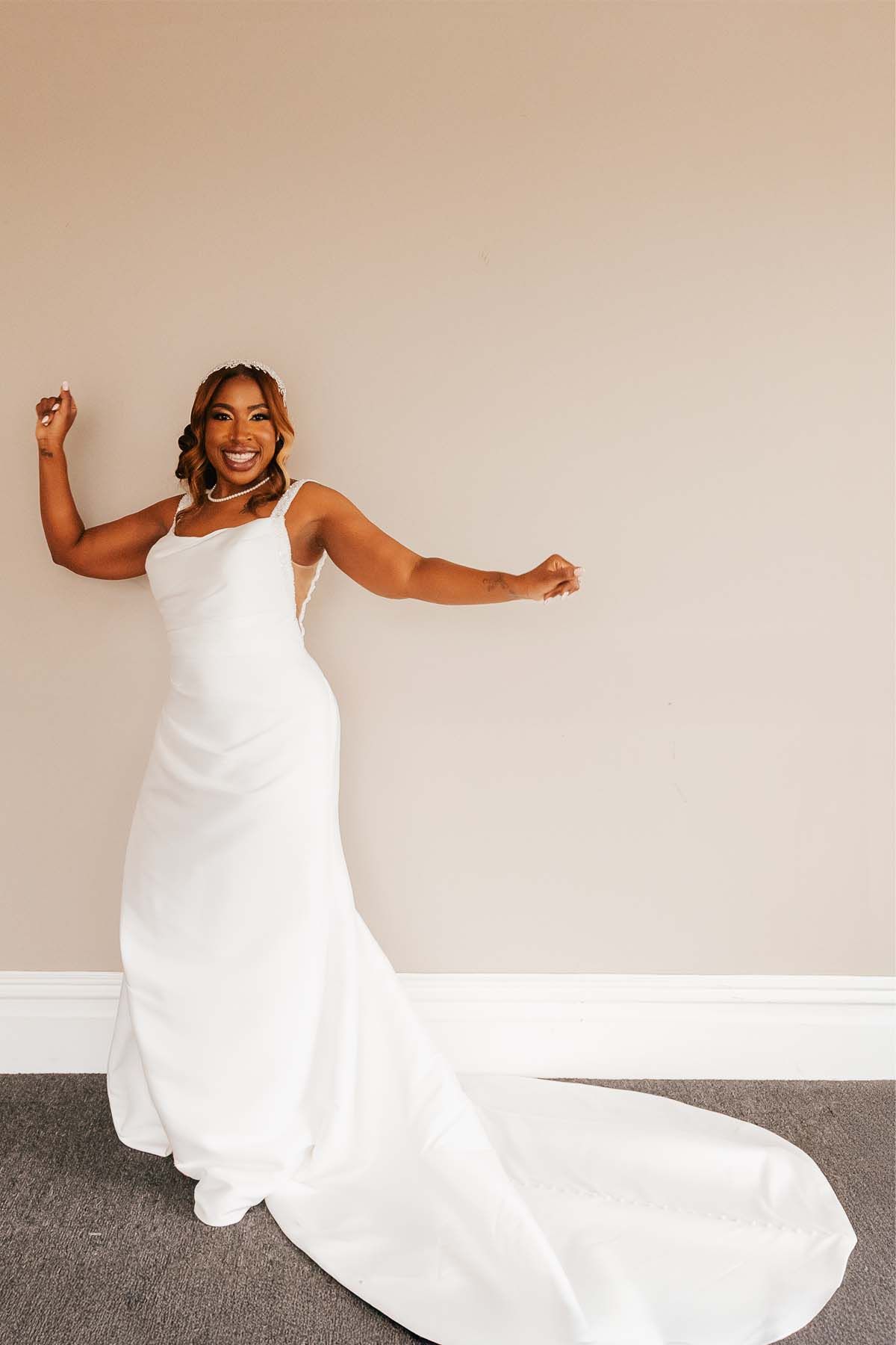 Bride in flowing white gown poses playfully against neutral background.