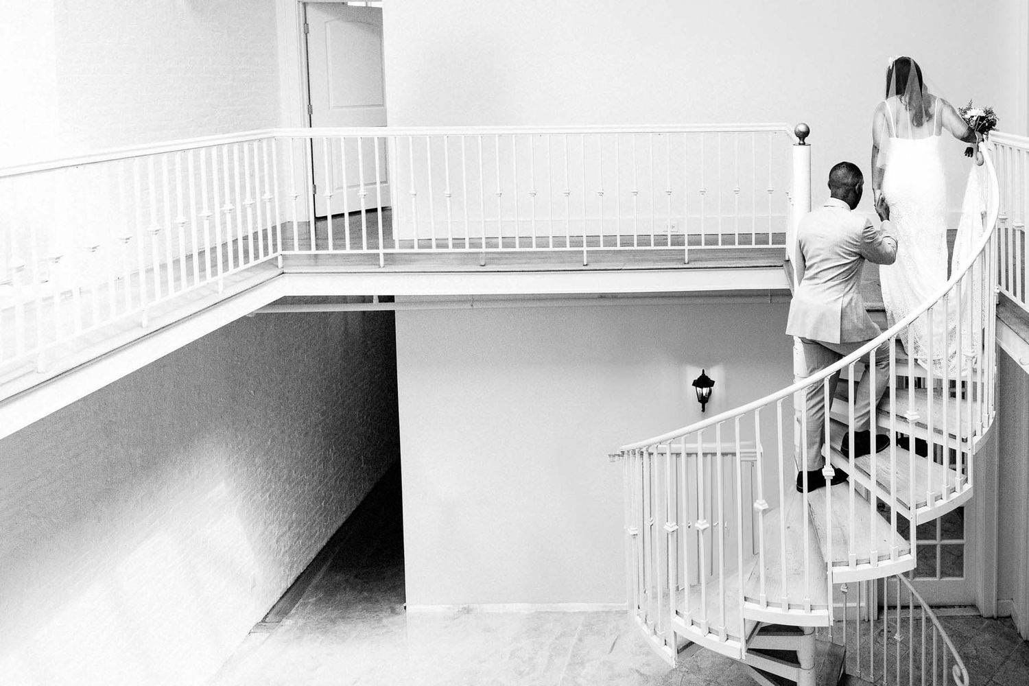 Black and white sequence of a bride and groom walking up a staircase in an elegant venue.