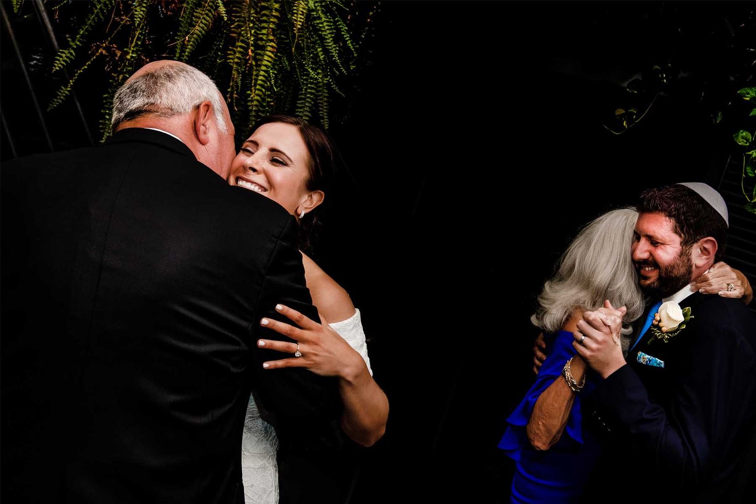Candid reception moments captured in dramatic low light setting with greenery.