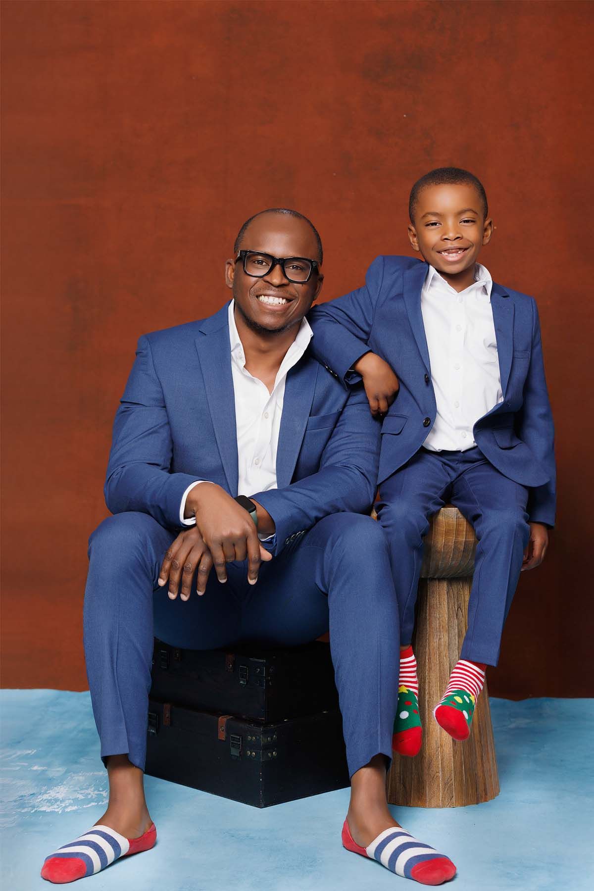 Father and son wearing matching blue suits and fun socks pose together.