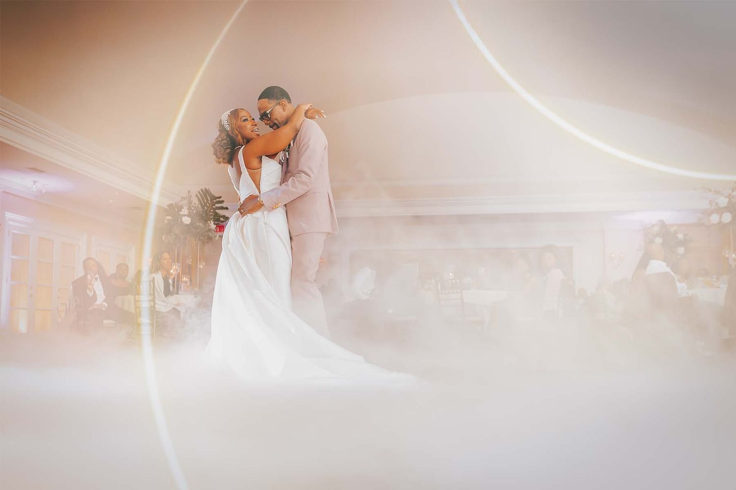Romantic dance floor moment with soft lighting and smoke effects at a wedding reception.