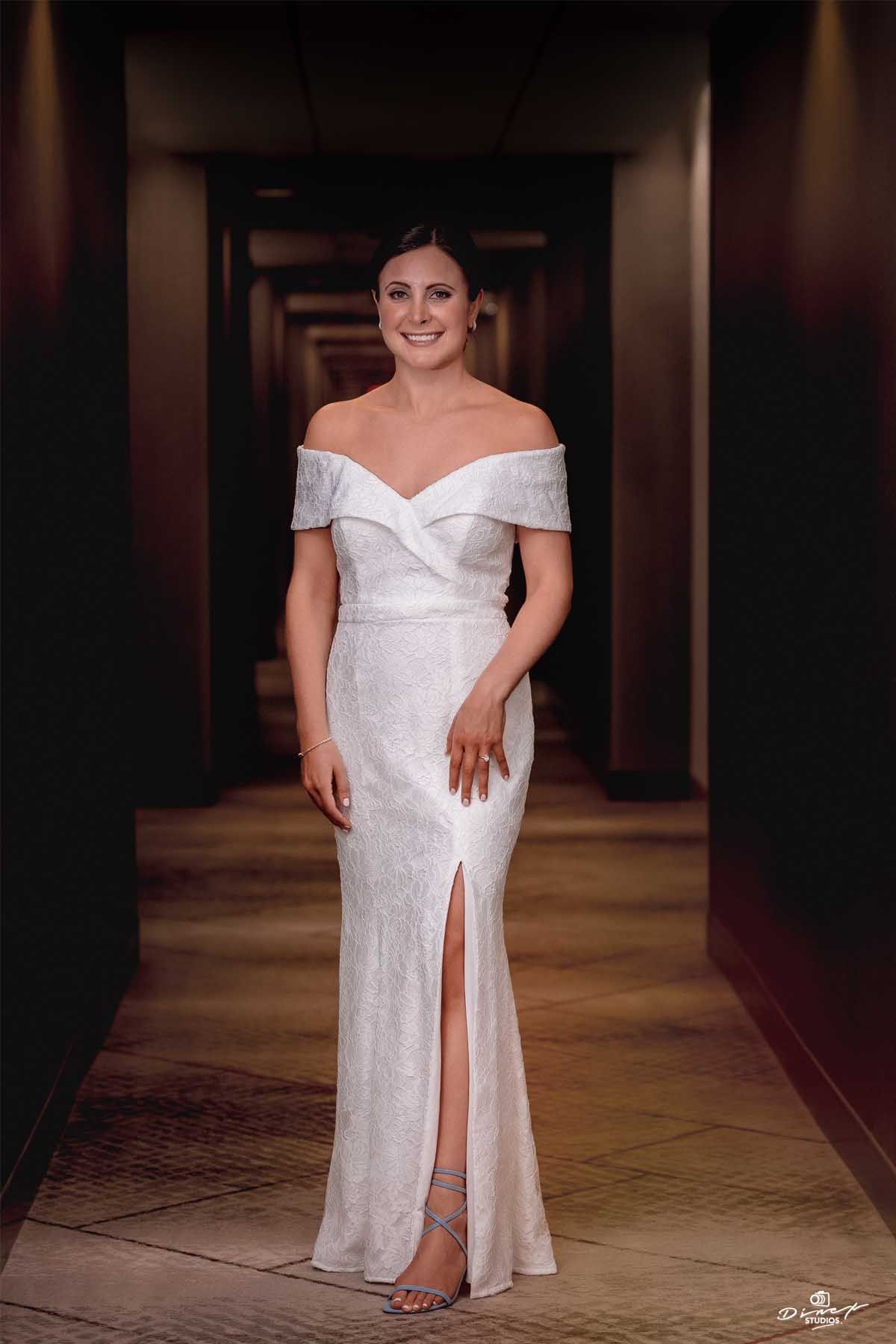Elegant off-shoulder wedding dress with side slit photographed in hallway setting.