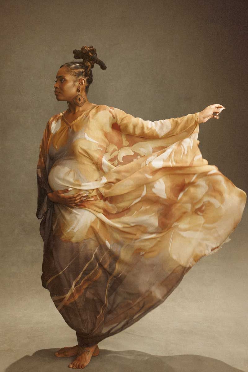 A figure in flowing peach fabric creates dramatic movement against a neutral studio backdrop.