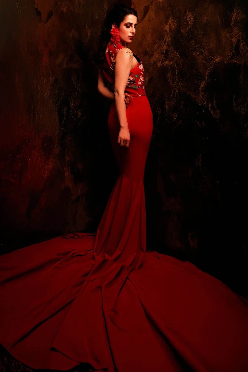 Elegant portrait of someone in a dramatic red mermaid gown against a dark textured background.