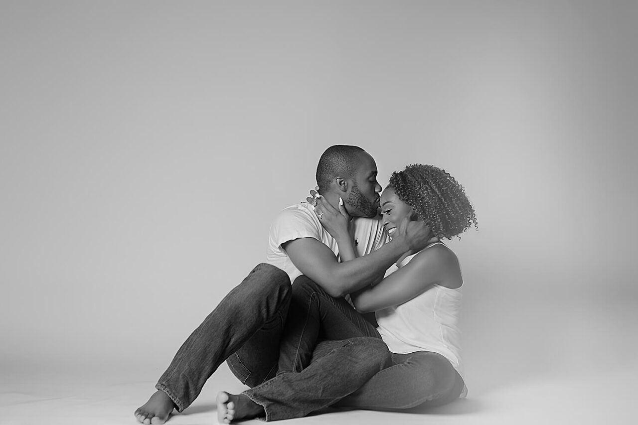 Artistic black and white portrait of couple embracing on studio floor.