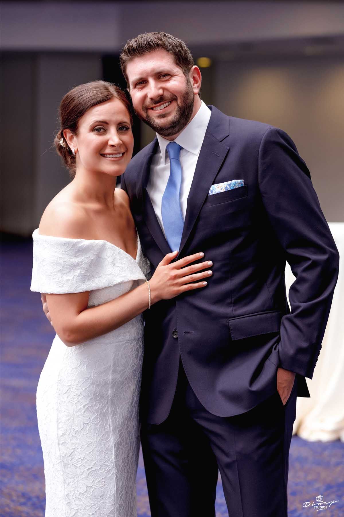 A couple in wedding attire posing together against a blue patterned background.
