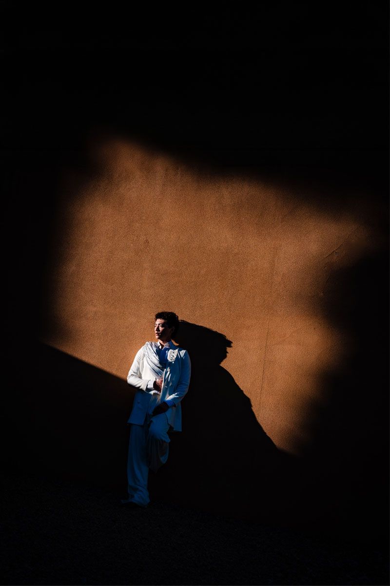 Dramatic lighting creates a striking shadow as someone poses against a warm-toned wall.