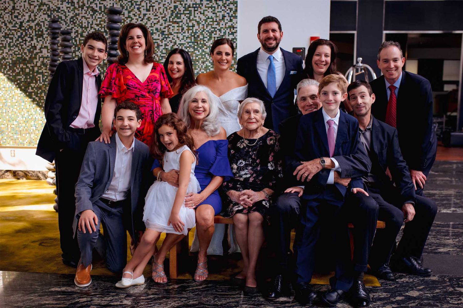 Large wedding party poses together outdoors for a group photo on stone steps.