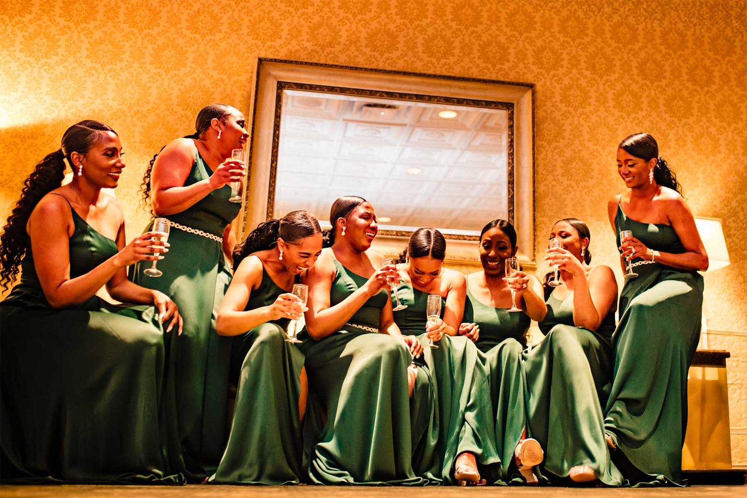 Bridesmaids in emerald green dresses sitting in a row at a wedding reception.