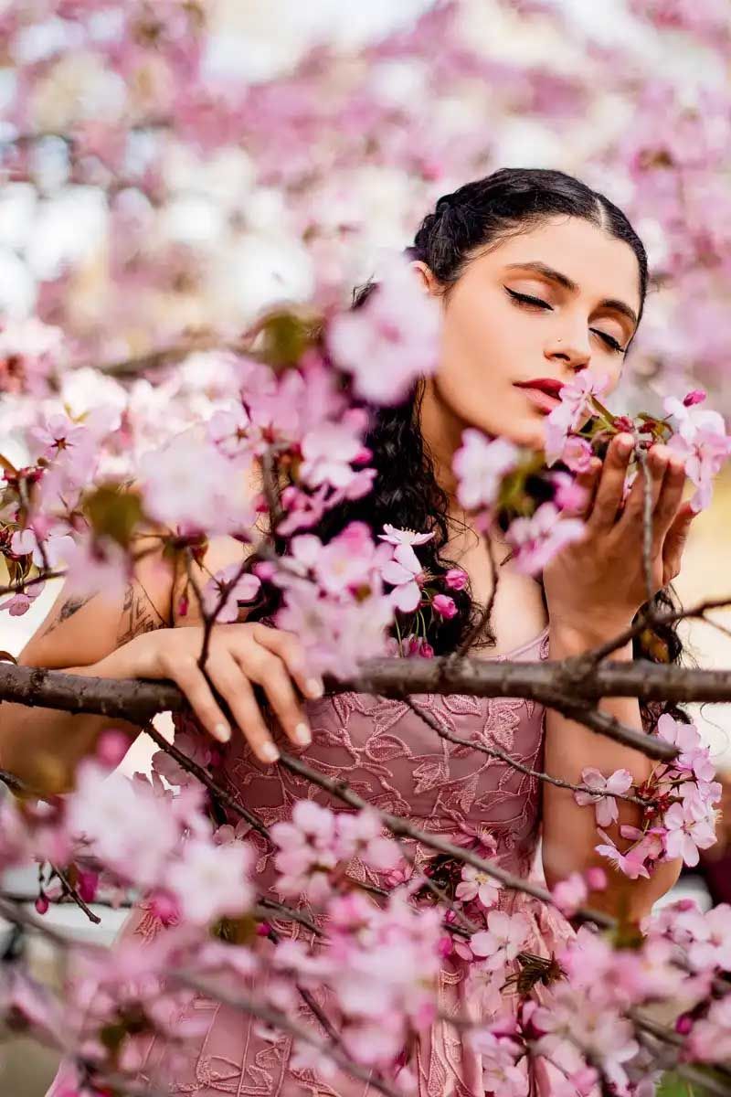 Romantic portrait amid pink cherry blossoms with model in pink dress.