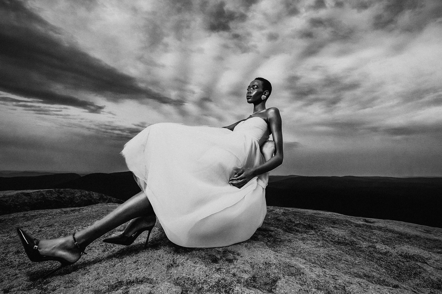 Dramatic black and white photo of figure with billowing white fabric on rocky outcrop.