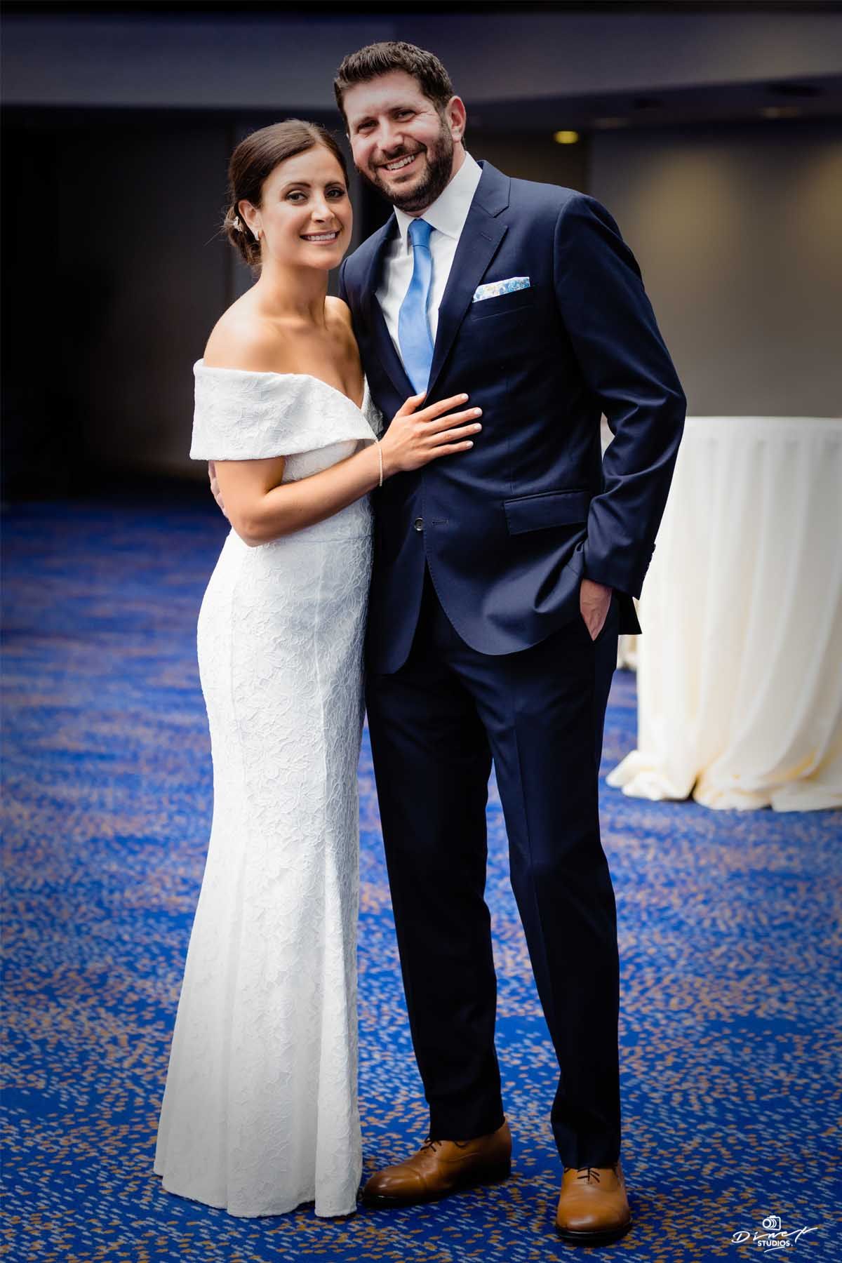 Wedding couple poses together on blue patterned carpet in formal attire.