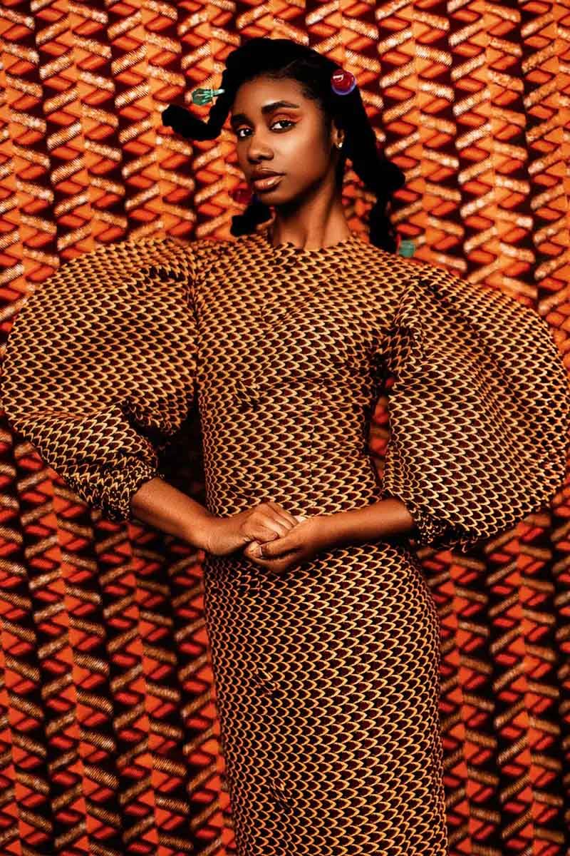 Fashion portrait against geometric pattern backdrop wearing polka dot dress with statement sleeves.