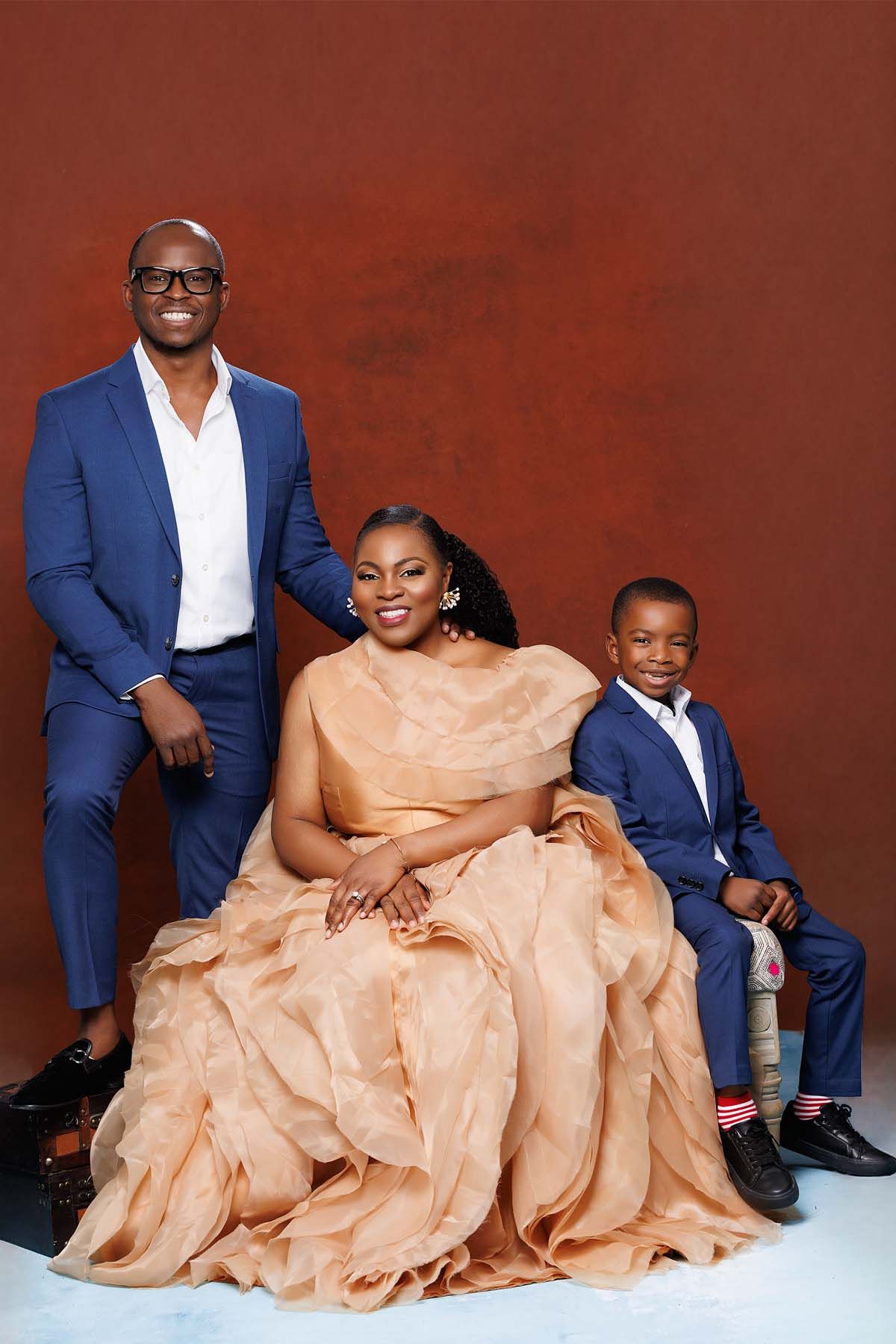 Family portrait with matching navy and peach formal attire against red backdrop.
