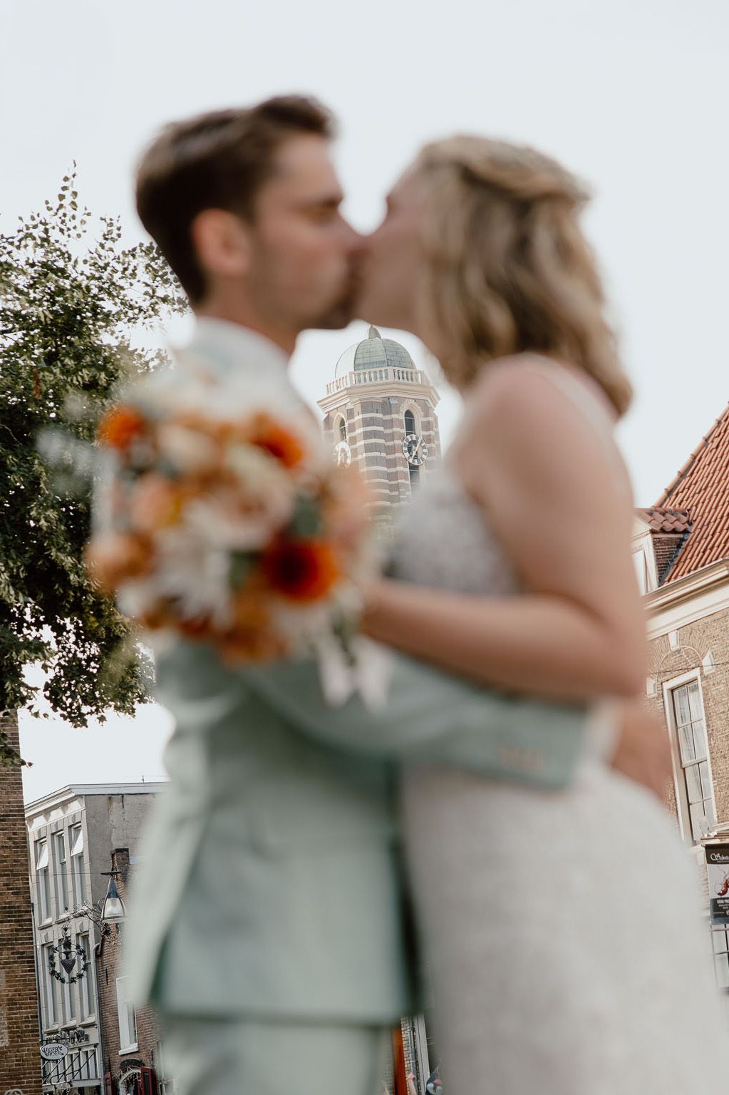Bruidspaar geeft elkaar een kus met een zomers trouwboeket en kerk op de achtergrond