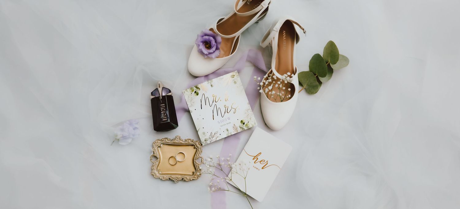 Flatlay van trouw details tijdens de voorbereiding van trouwdag. Je ziet de trouwschoenen, parfum, ringen, uitnodiging en bloemen
