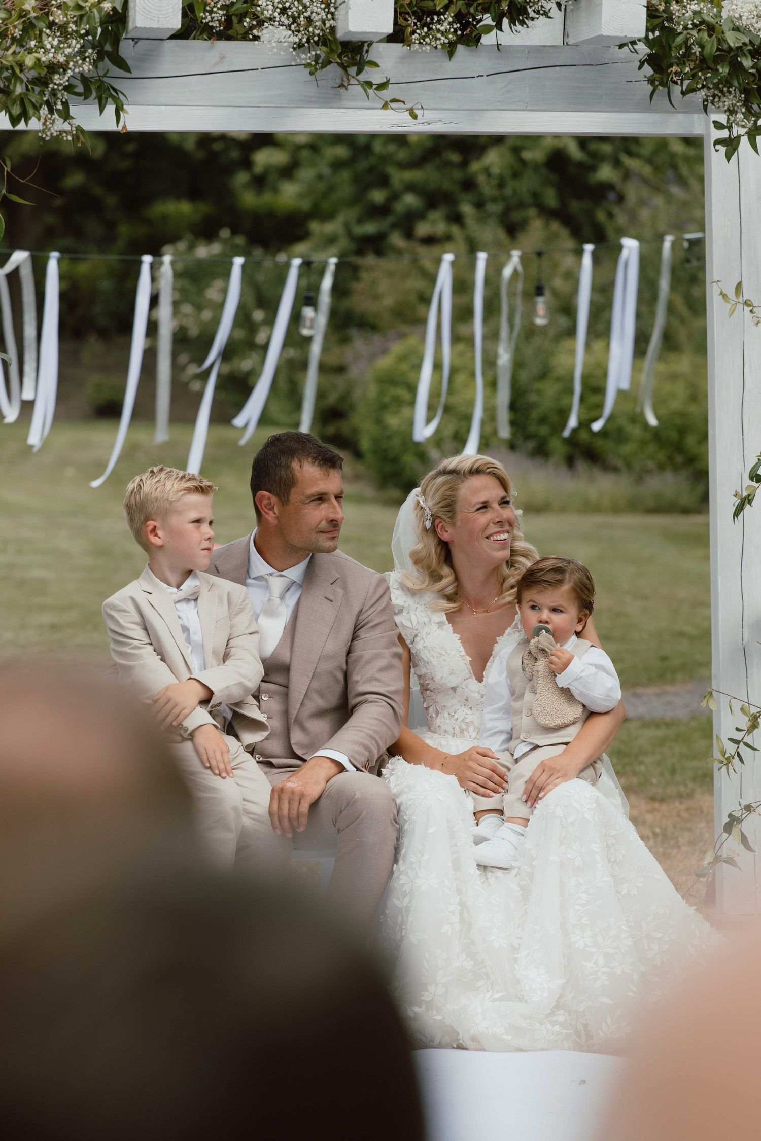 Het bruidspaar met kinderen op schoot tijdens de ceremonie - spontane trouwfotografie in Almere, Flevoland.