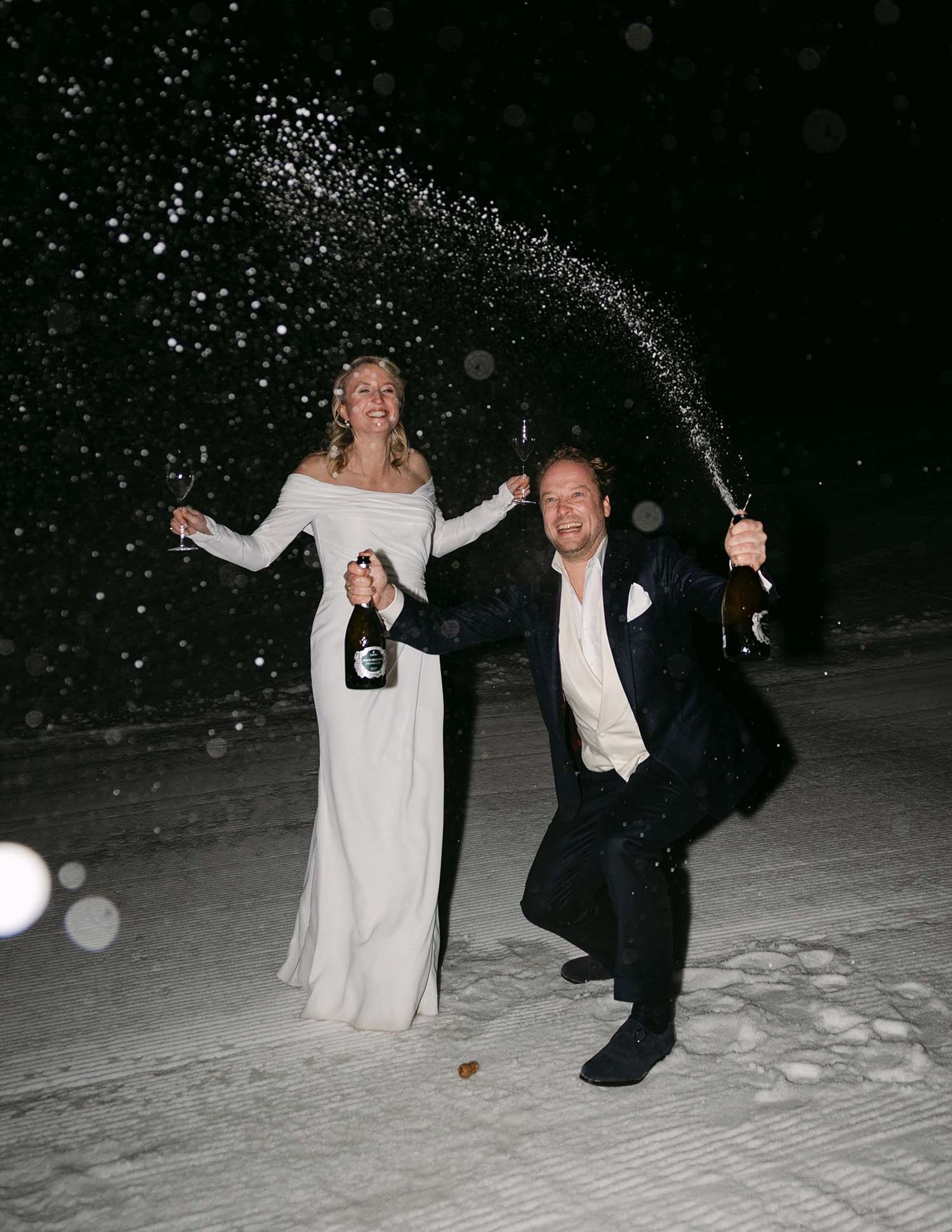 Bruidspaar spuit met champagne flessen om hun trouwdag te vieren in de sneeuw