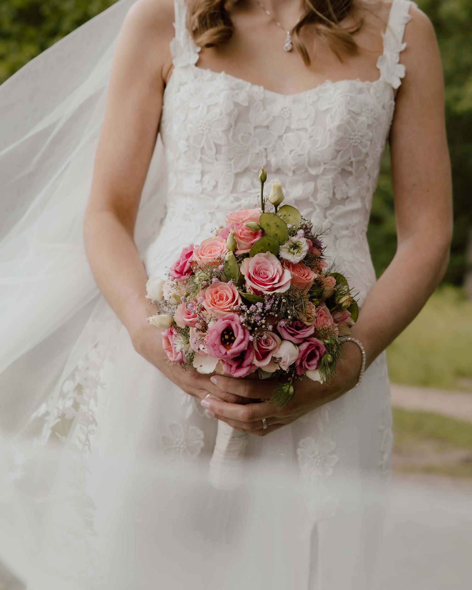 Bruid in trouwjurk houdt trouwboeket met roze bloemen vast en een zachte sluier
