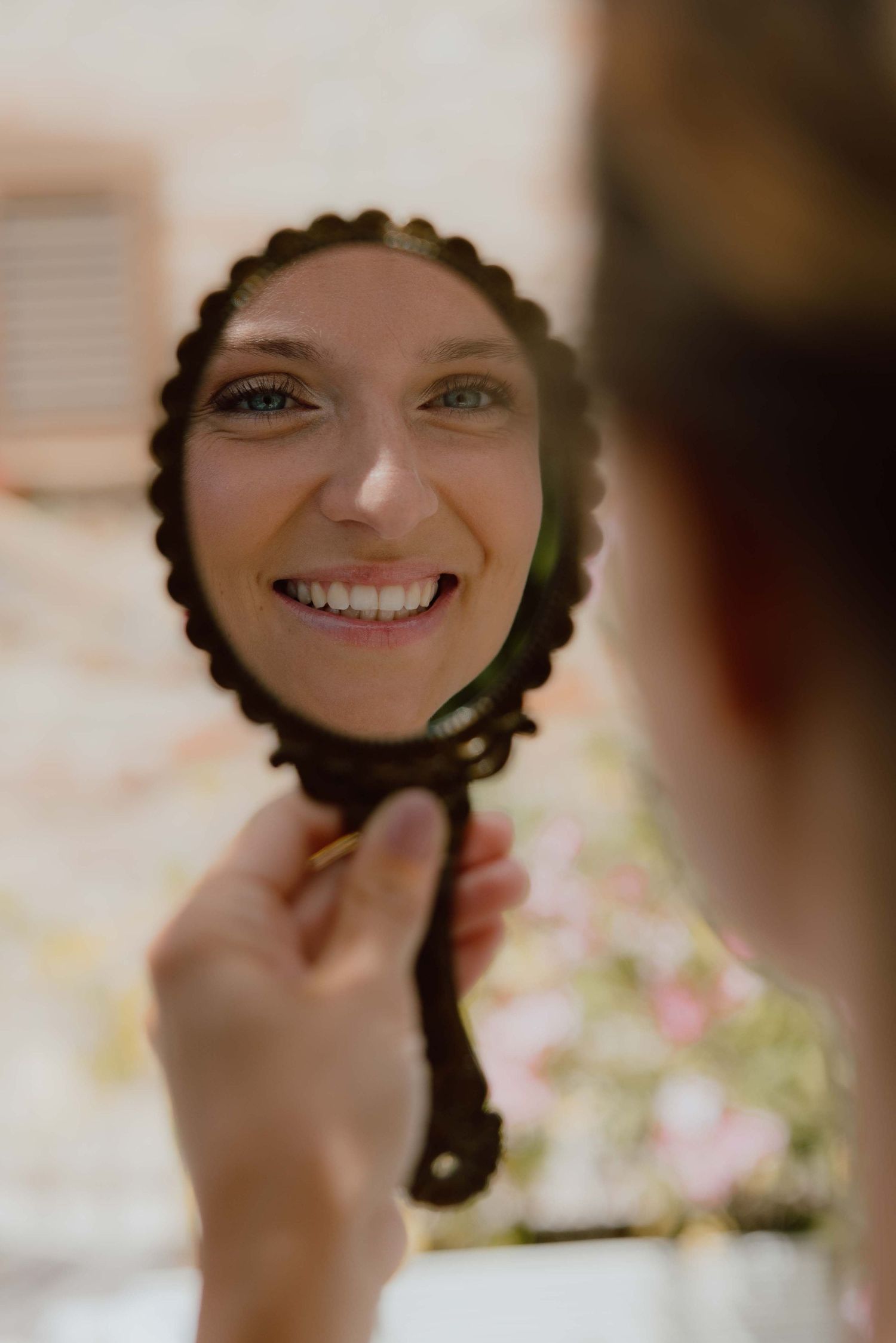 Lachende bruid kijkt naar een vintage spiegel om haar make-up te bekijken