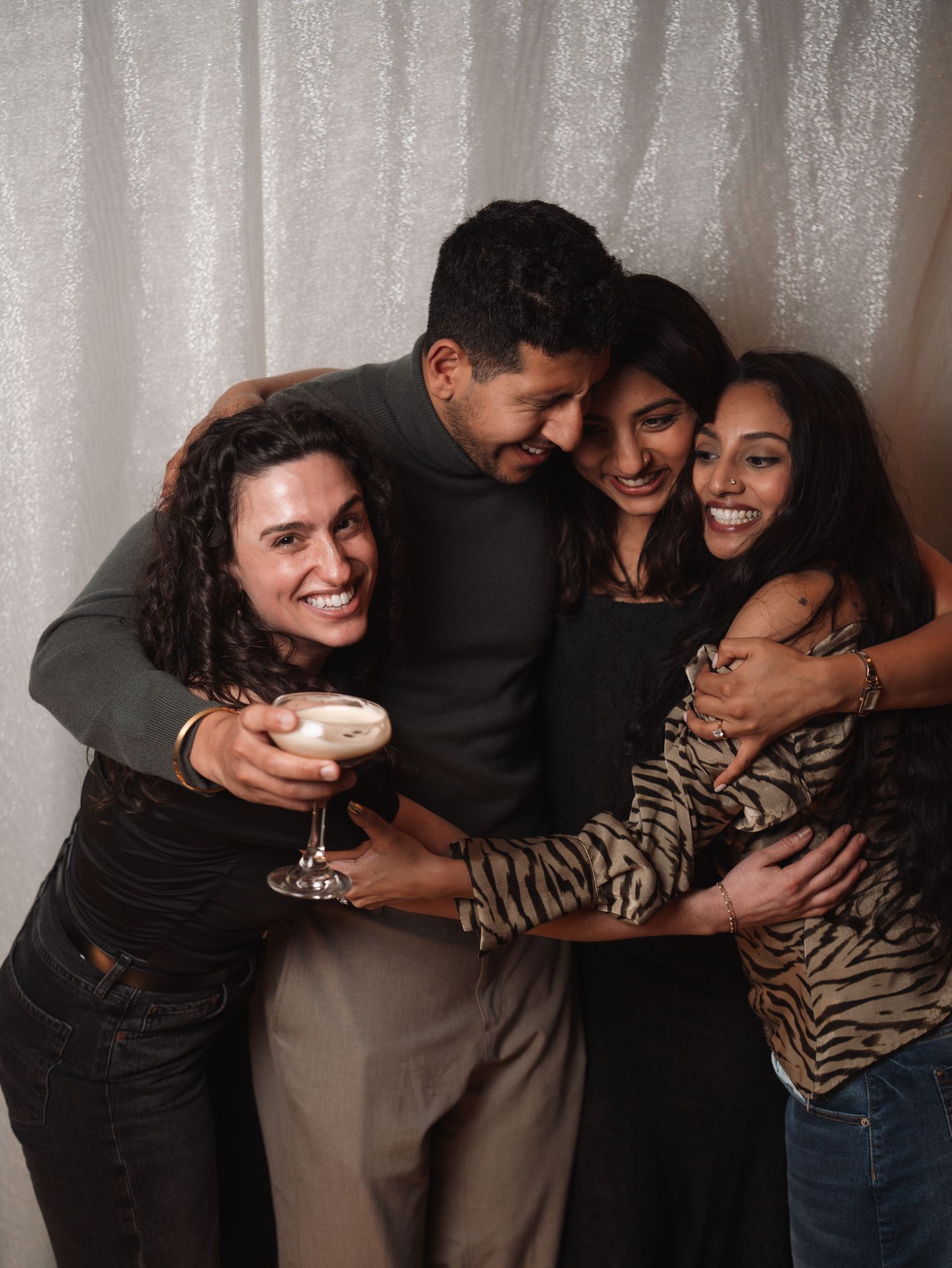 Group of four friends laughing and embracing together at a party photo booth.