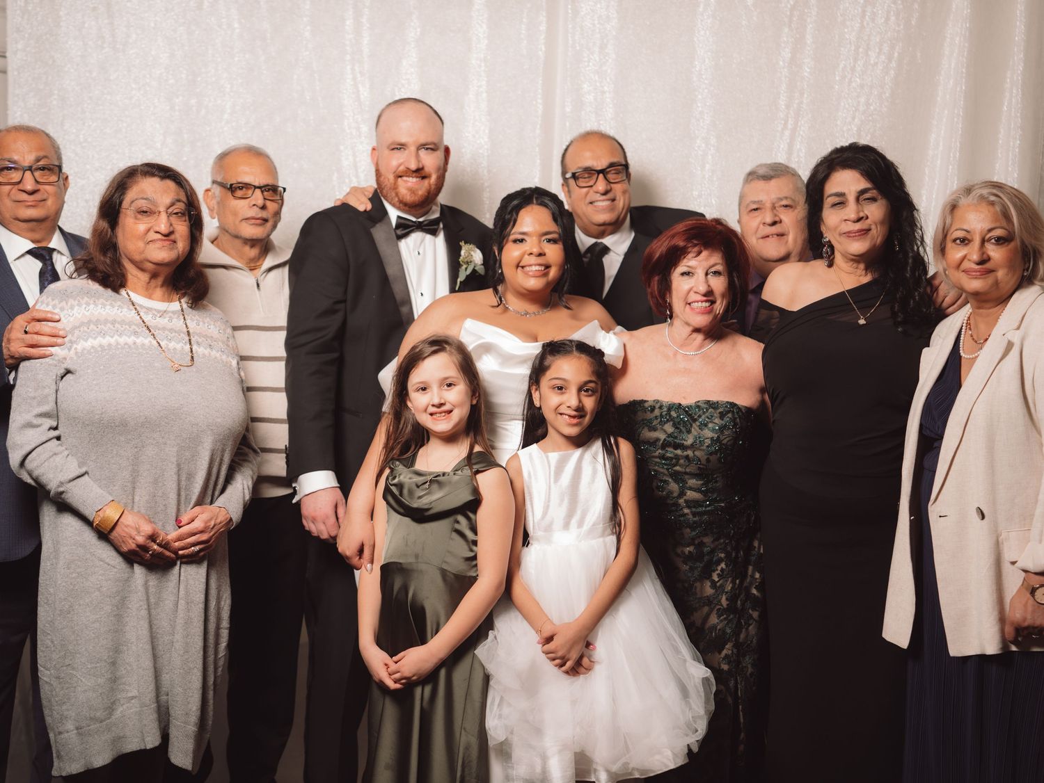 Bride and groom pose with large multigenerational family group at elegant wedding reception.