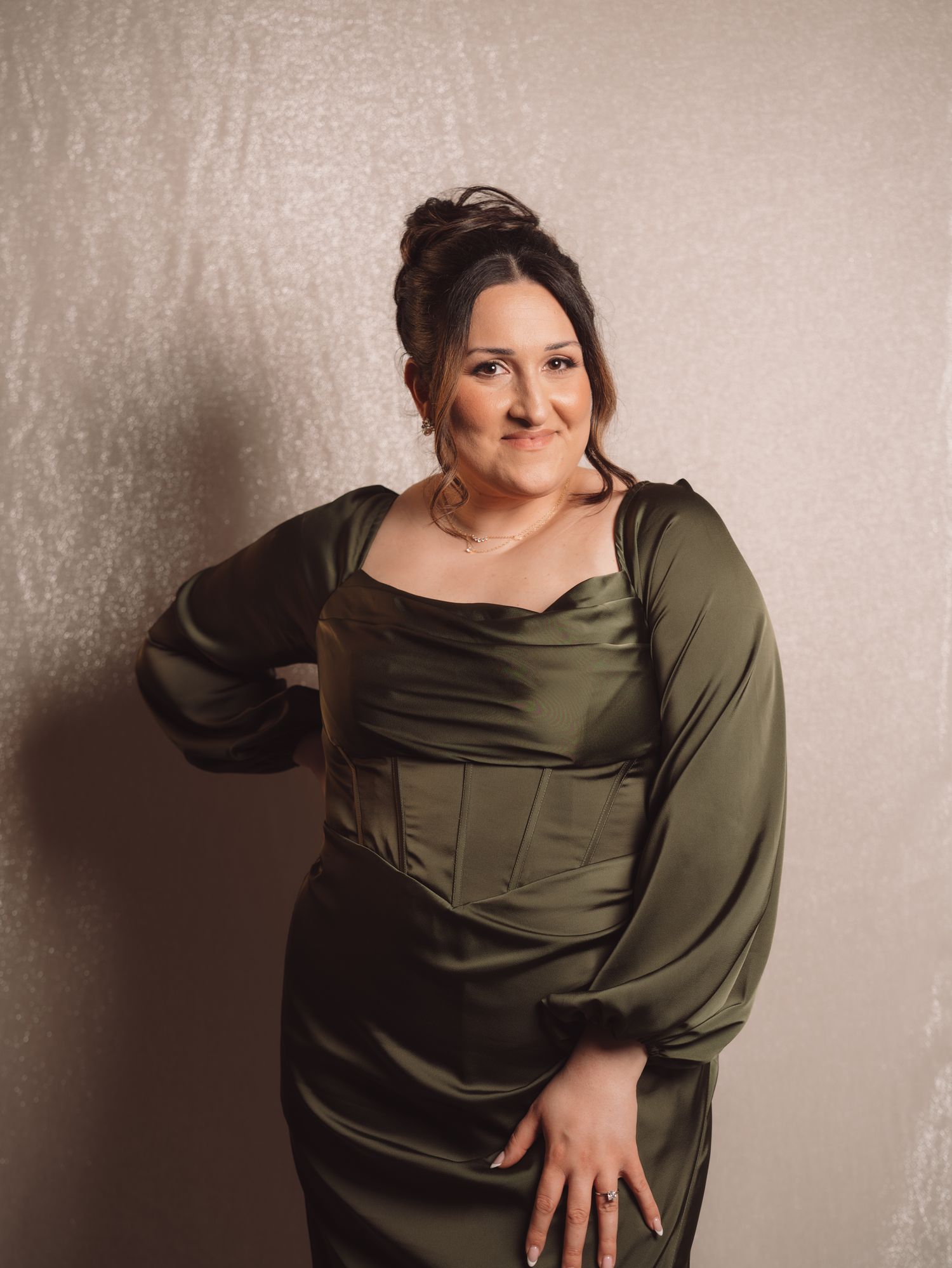 Woman posing confidently in an elegant olive green satin gown at a formal event.