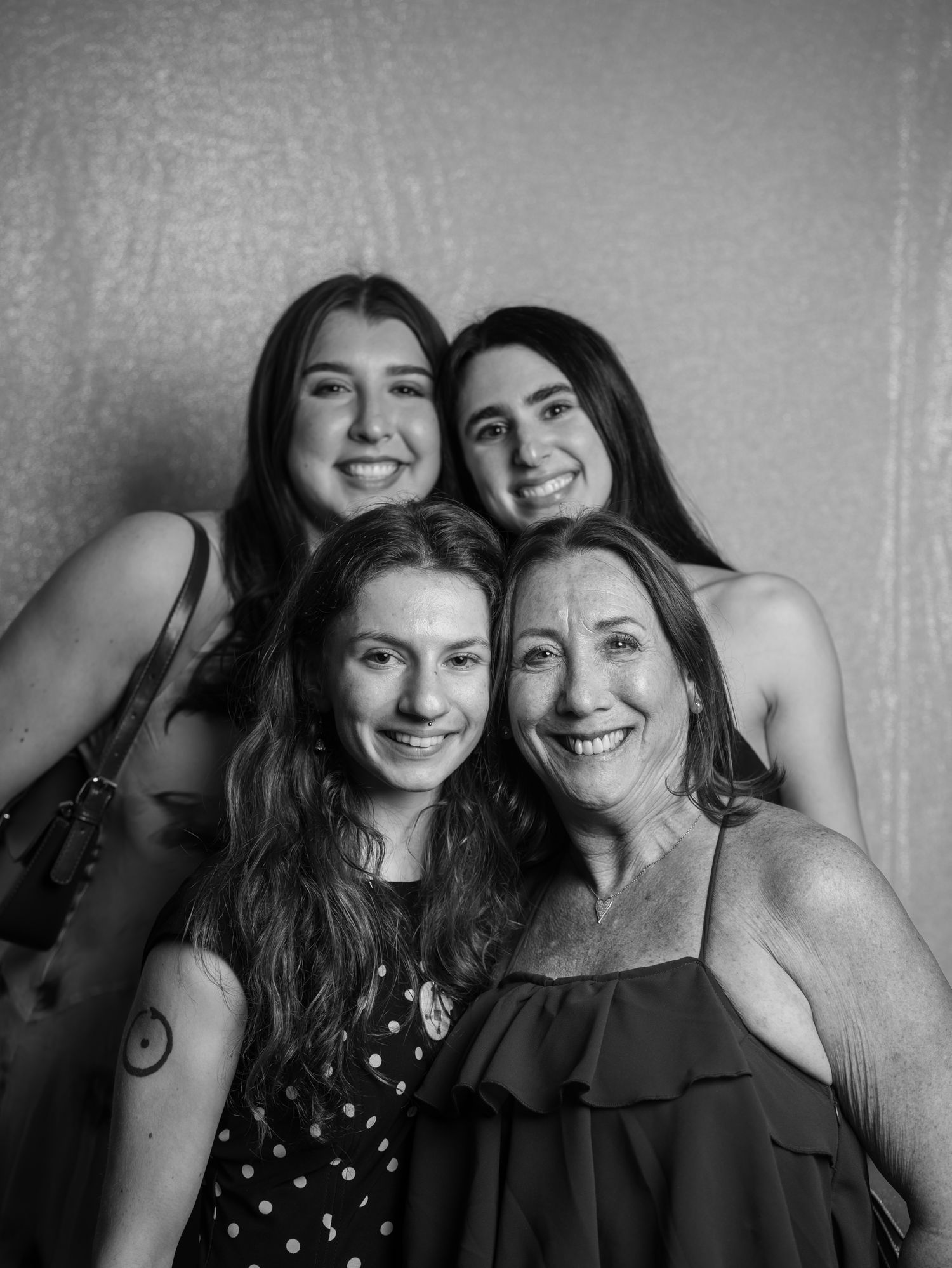Black and white portrait of four women smiling together at a wedding reception.