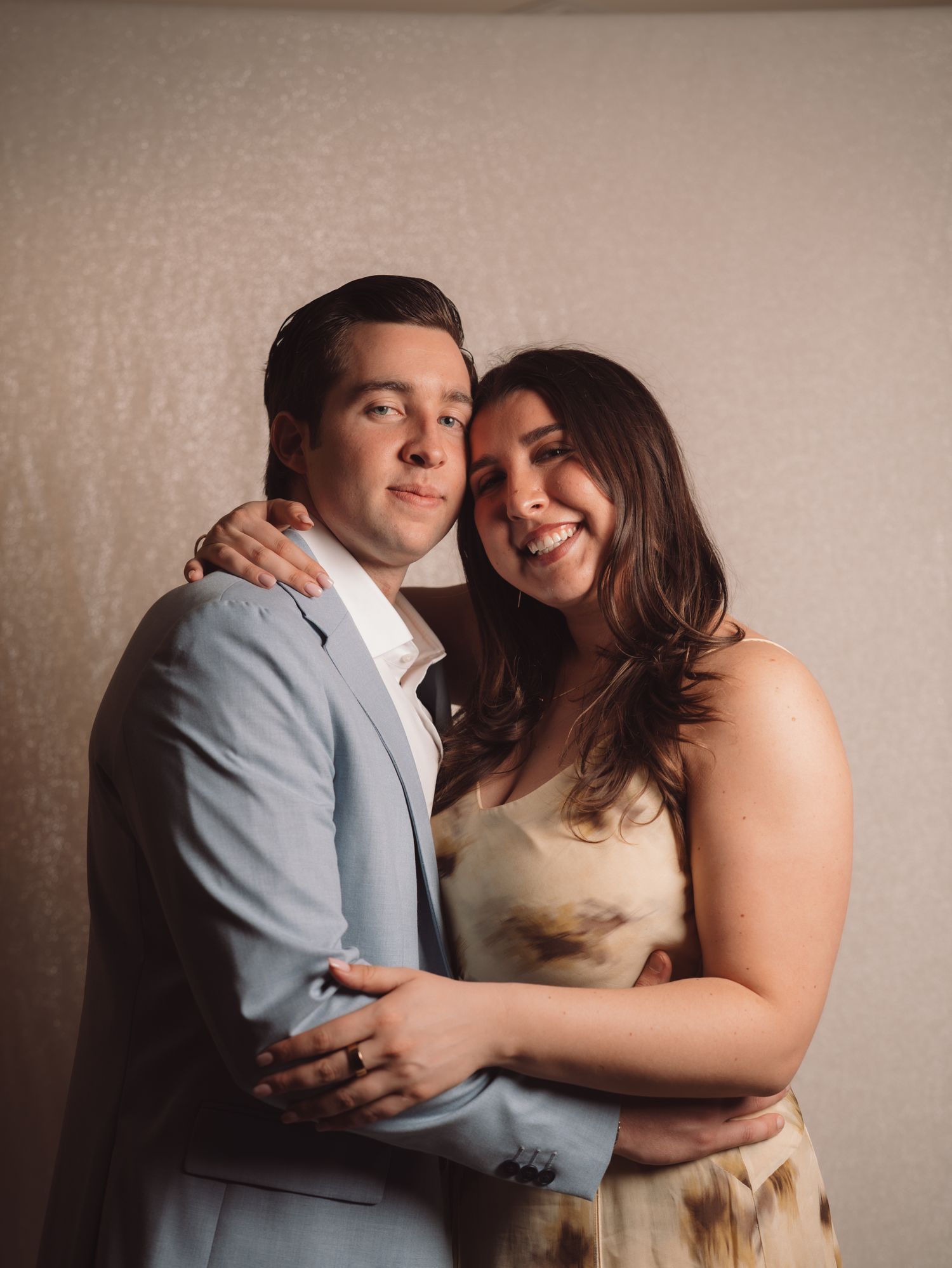 Couple embracing and smiling together at a wedding reception, man in light blue suit and woman in floral dress.