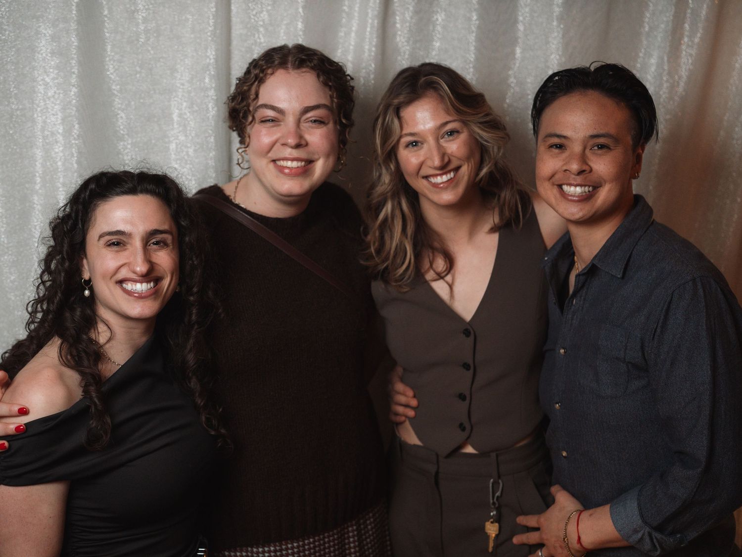 Four young women smile and pose together at a casual wedding reception gathering.