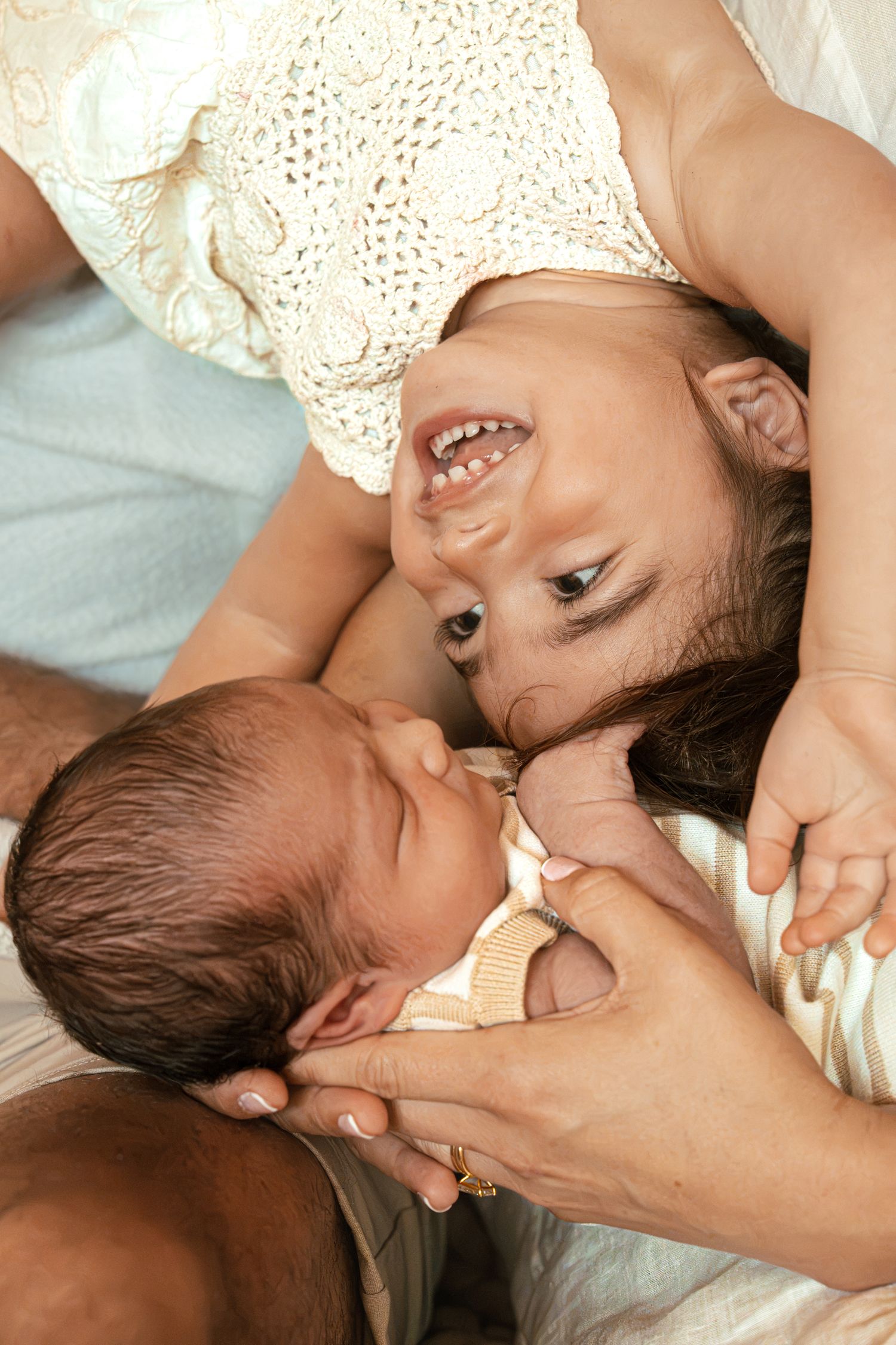 A joyful mother lying down smiles warmly at her sleeping newborn baby held gently in loving hands.