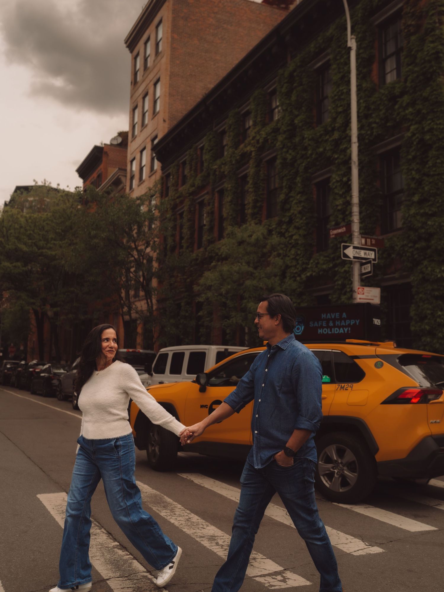 Couple holding hands crossing a zebra crossing in New York City with a yellow taxi cab in the background.