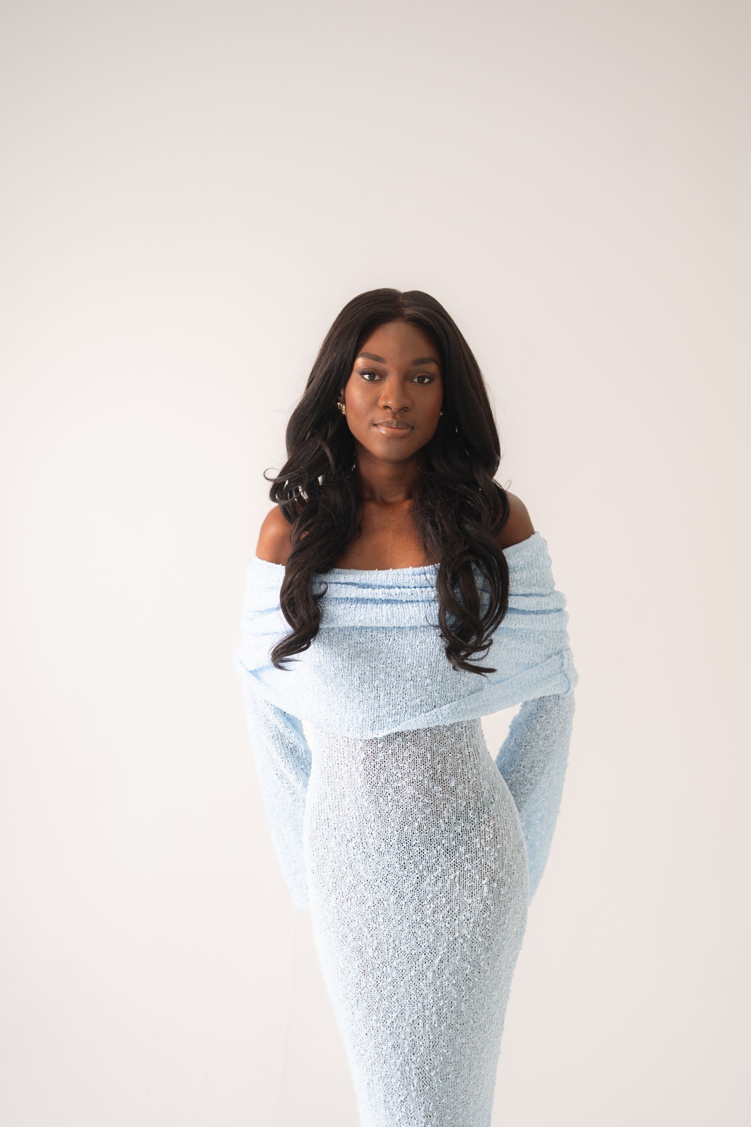 Young woman in light blue off-shoulder knit maxi dress posing against white background.