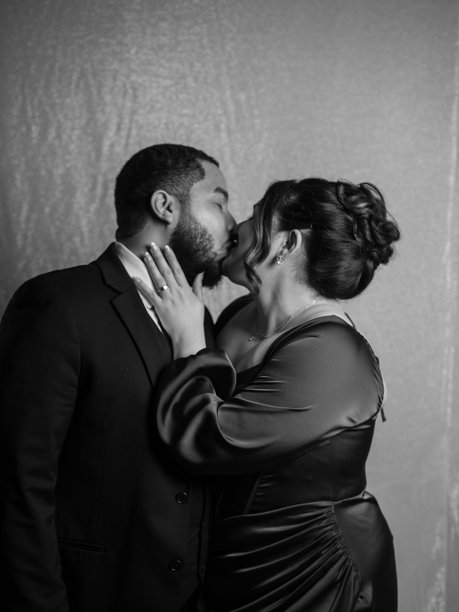 Black and white photo of a couple sharing a romantic kiss at a wedding celebration.