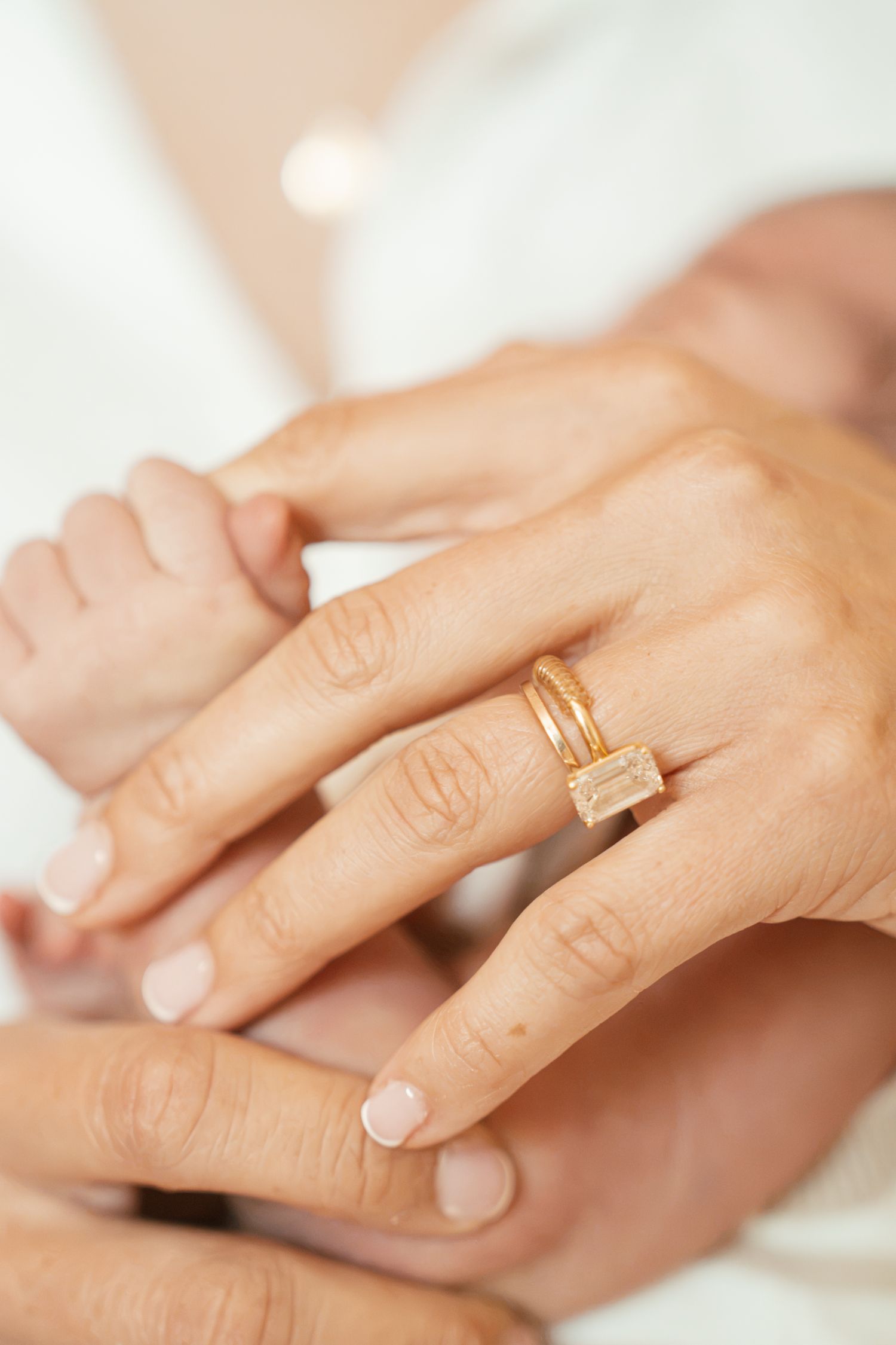Close-up of a woman's hand wearing a gold rectangular gemstone ring, gently holding a newborn baby's tiny feet.
