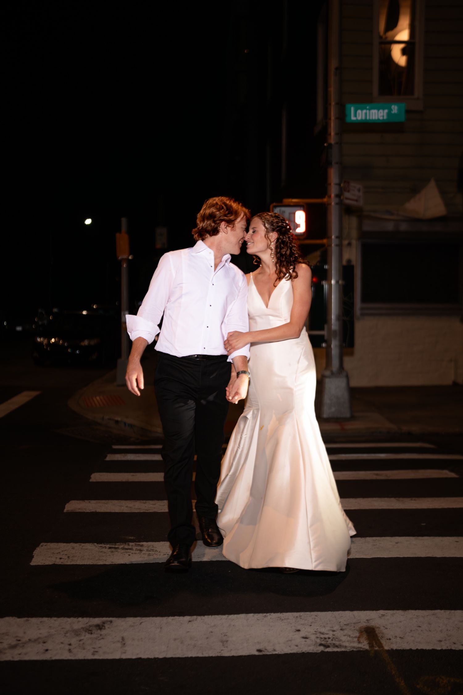 Newlywed couple kissing while crossing a street at night near Lorimer Street sign in Brooklyn.