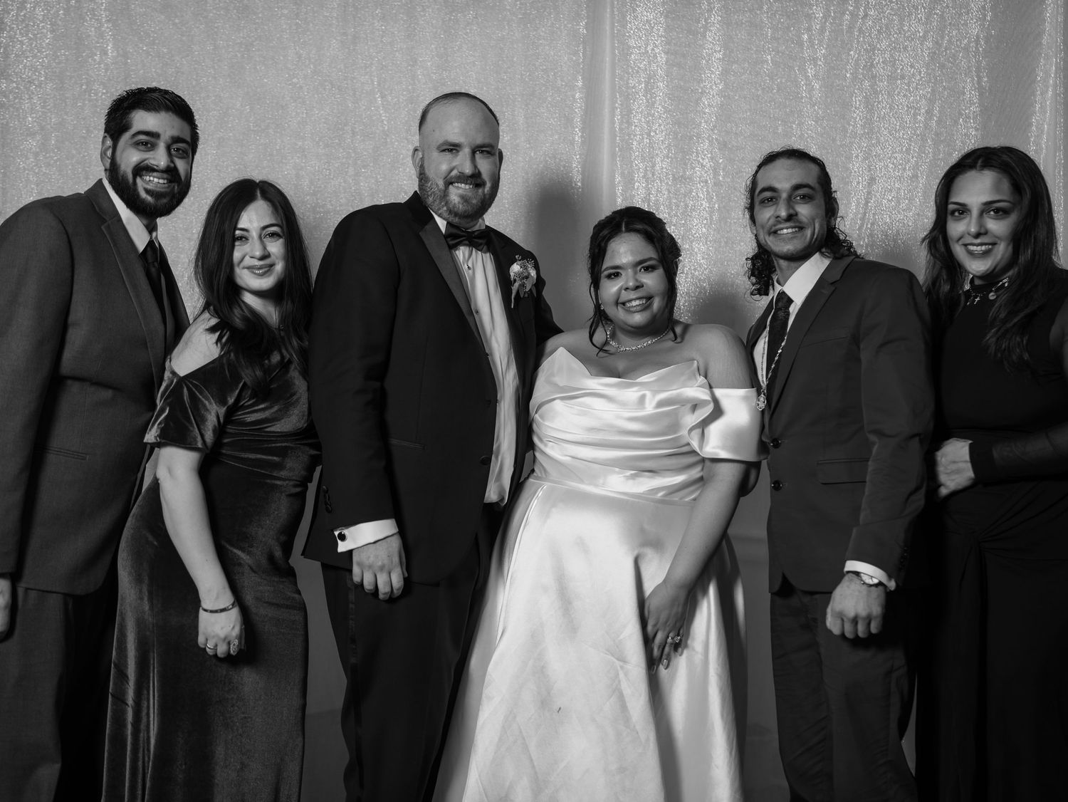 Black and white group portrait of bride in white gown with five formally dressed wedding guests.