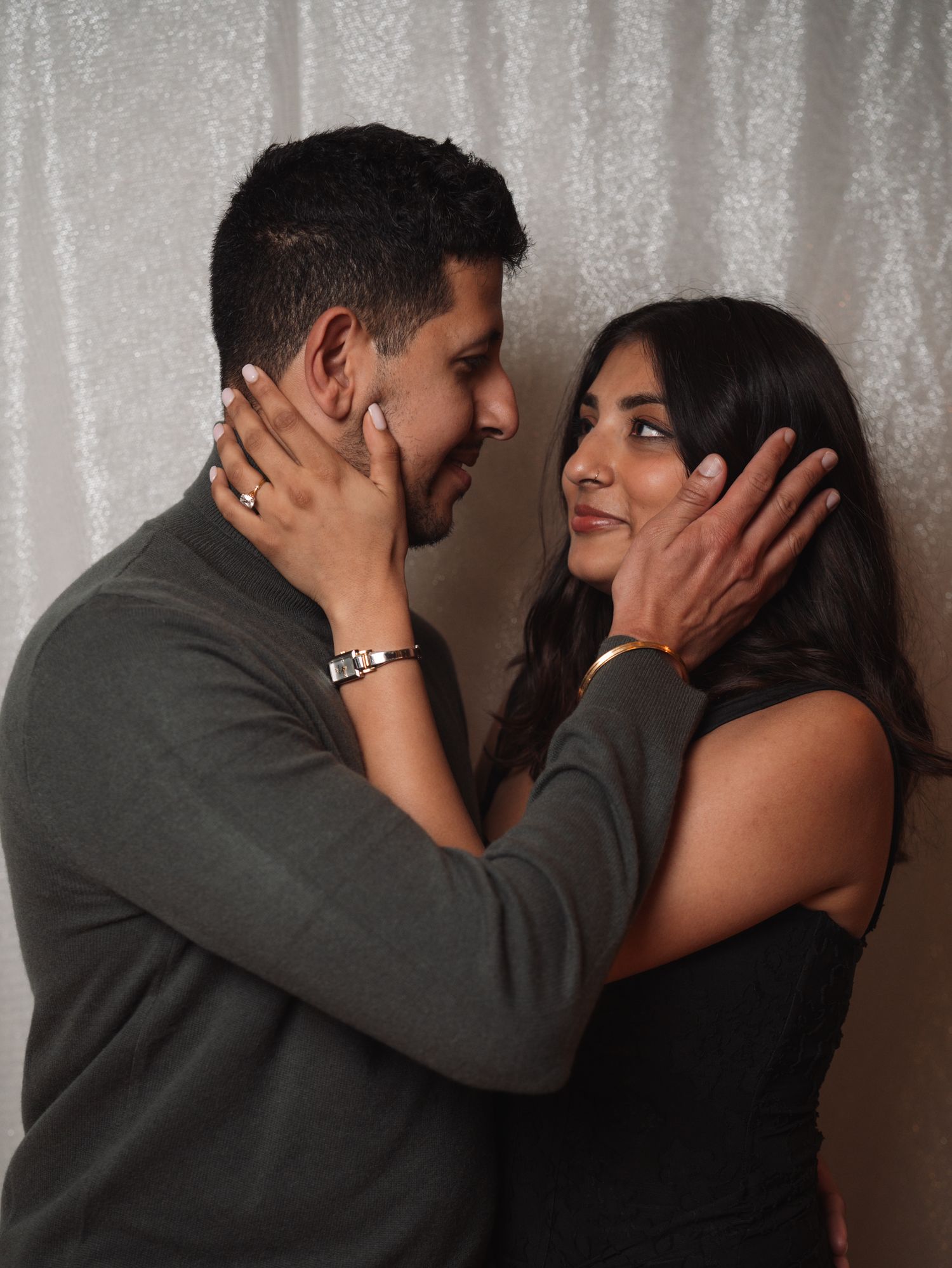 Couple sharing a tender moment holding each other's faces at a sparkly backdrop.