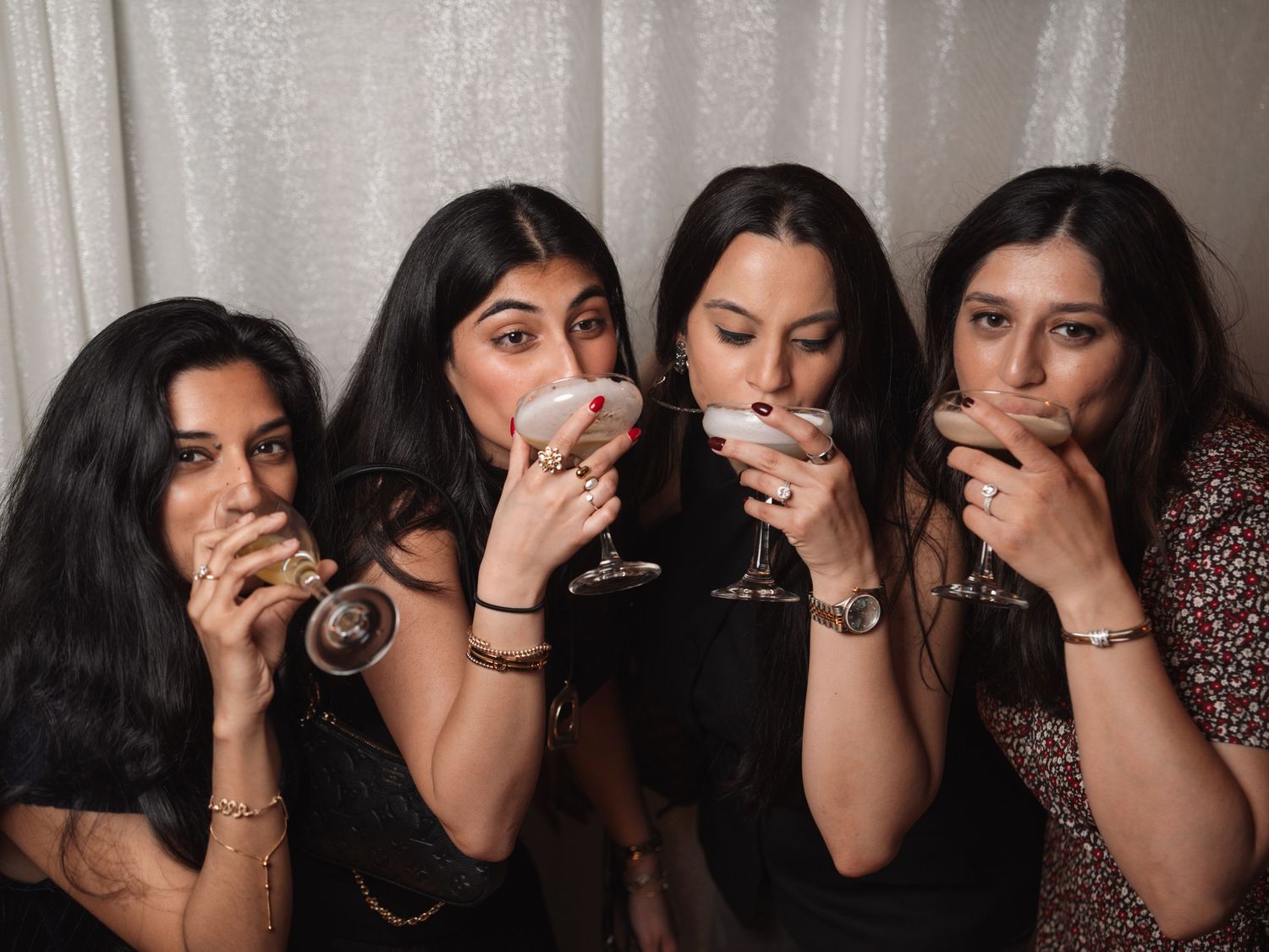 Four women sip cocktails together in a fun candid photo at a wedding reception.