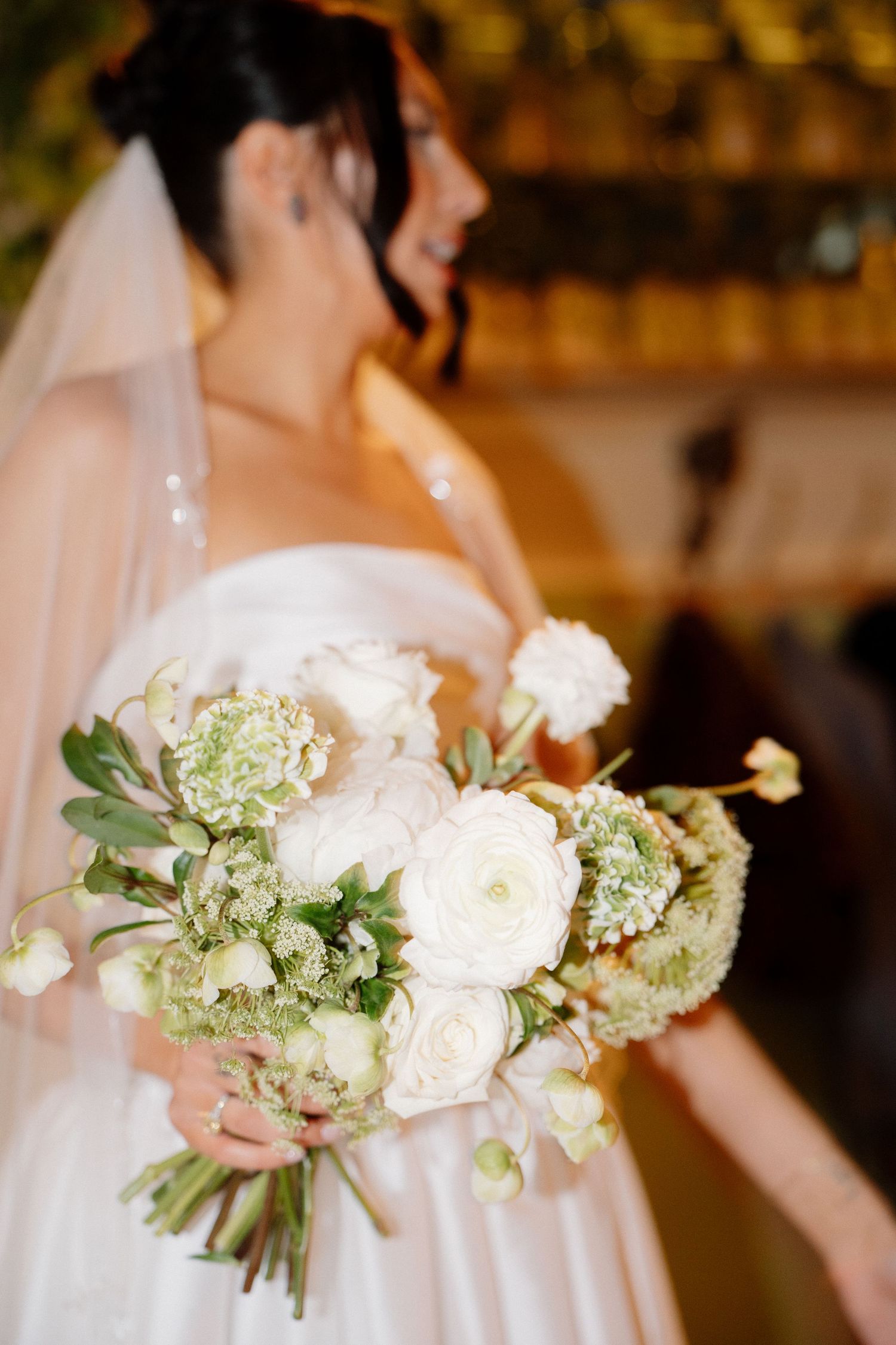 Smiling bride in strapless white gown holding a lush bouquet of white roses and green flowers with veil.