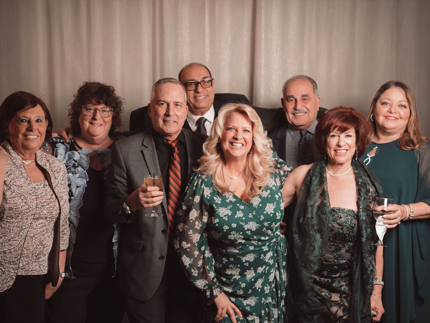 Group of smiling wedding guests pose together holding drinks at a formal reception celebration.
