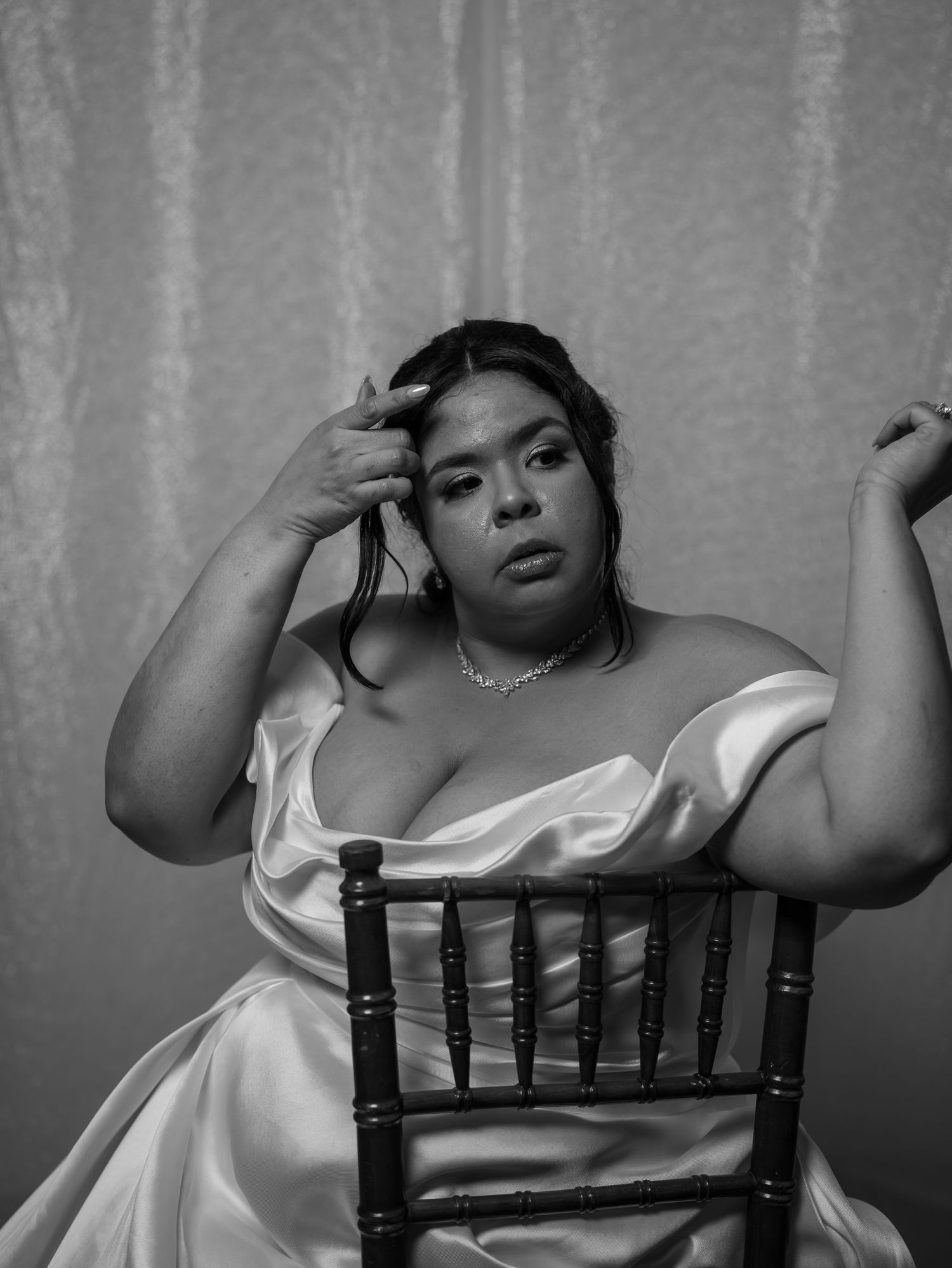 Black and white artistic portrait of bride in white satin gown seated on chiavari chair.