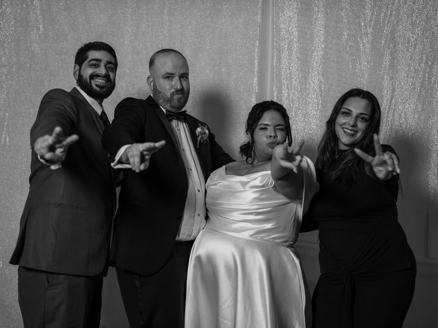 Black and white photo of bride and three guests pointing at camera at wedding reception.