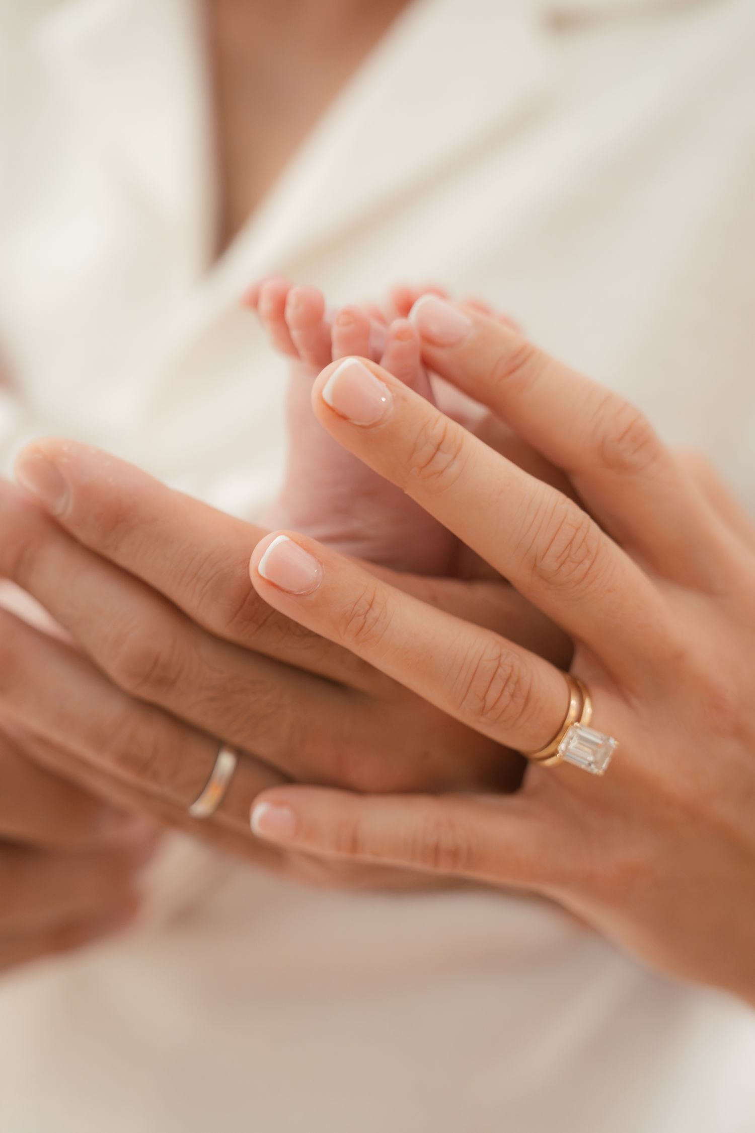 Close-up of adult hands with gold rings gently holding tiny newborn baby feet.