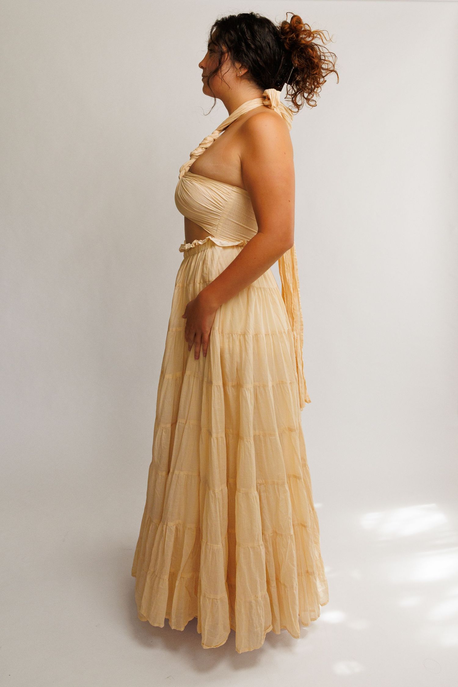 Woman wearing a flowing tiered halter gown in champagne gold, featuring ruched bodice and full skirt.